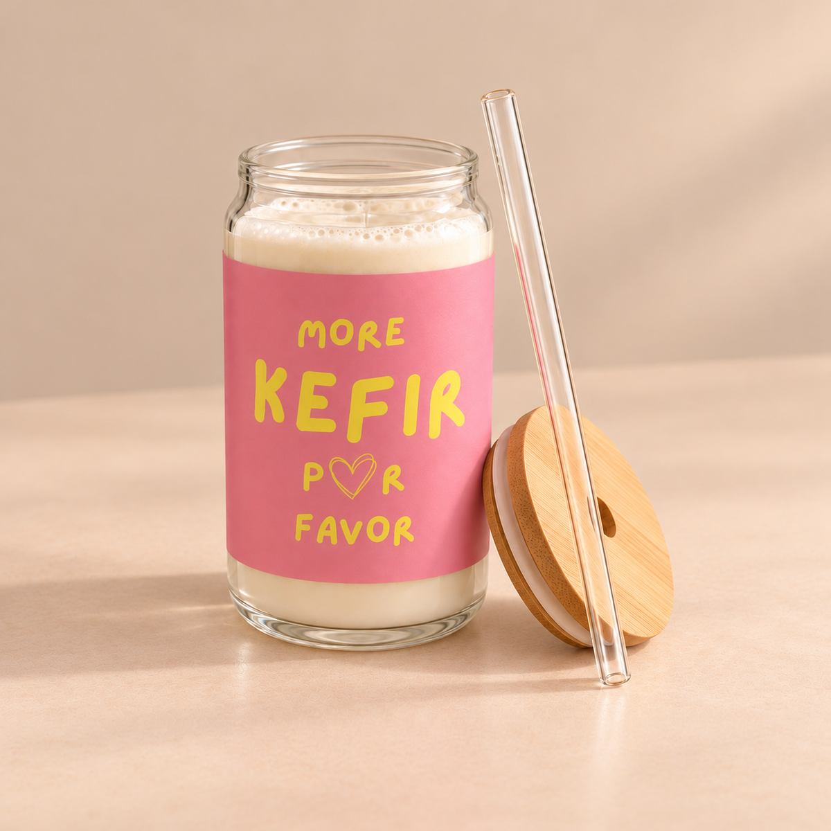 Rosa bedrucktes More Kefir Por Favor Trinkglas mit Milchkefir, daneben ein Bambusdeckel und ein transparenter Trinkhalm.