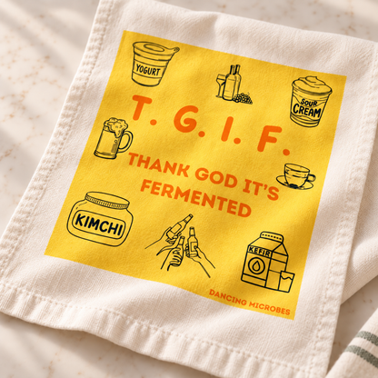 Nahaufnahme des gelben TGIF-Aufdrucks „Thank God It’s Fermented“ mit Illustrationen rund um Kefir, Kimchi und Fermentation auf einem Baumwoll-Geschirrtuch.